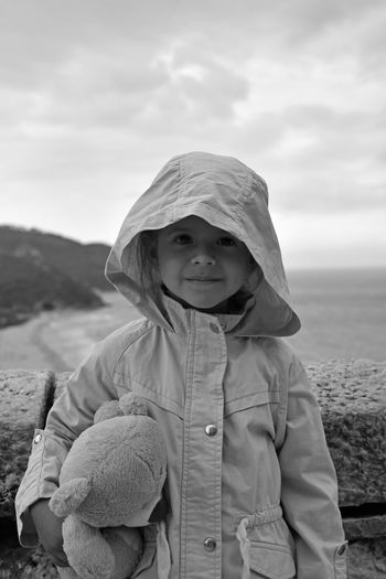 Portrait of smiling girl with teddy bear standing against sea