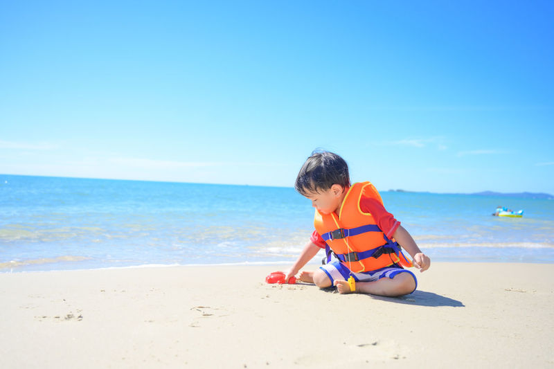 Side view of boy playing at beach against clear blue sky