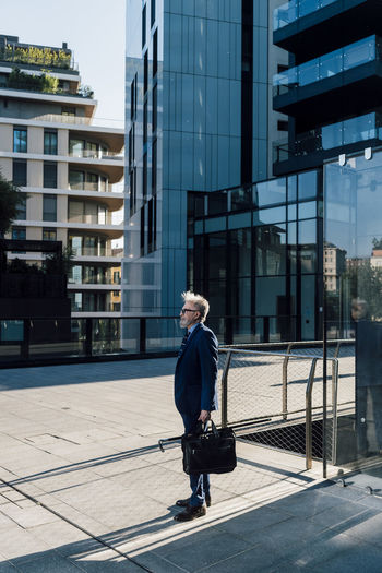 Senior businessman standing with briefcase outside office building exterior