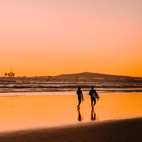 Men walking on beach against sky during sunset