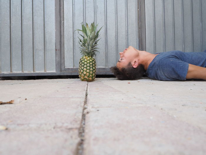 Surface level of young man looking at pineapple while lying on footpath