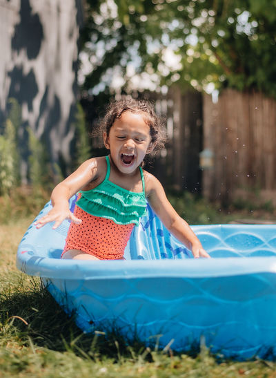 Mixed race young girl at home having fun on hot summer day in kiddie pool