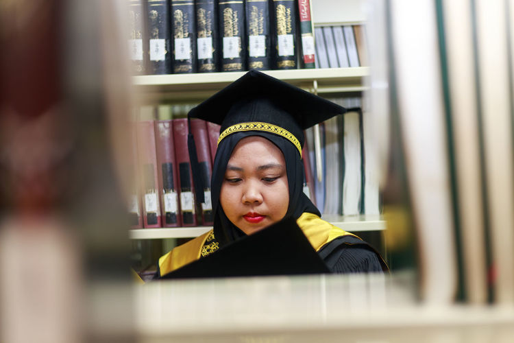 Young woman wearing graduation gown in library