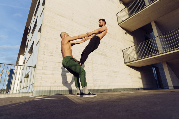 Young athletic shirtless men doing an urban workout outdoors practicing balance exercises