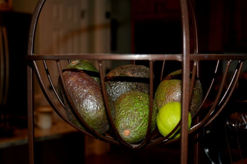 Close-up of avocados and a lime in metal basket on table