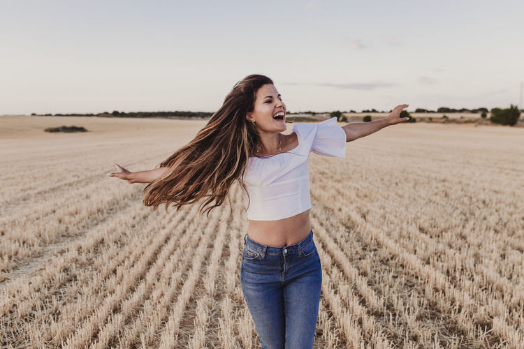 Carefree mid adult woman with arms outstretched standing on agricultural field