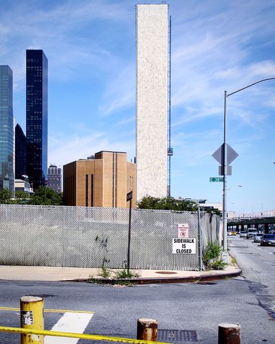 Road sign by modern buildings in city against sky