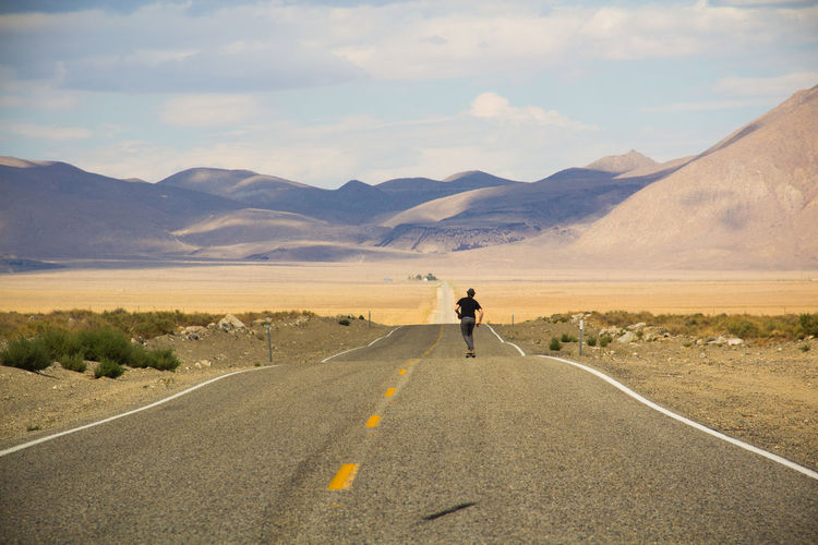 Rear view of man skateboarding on road at desert