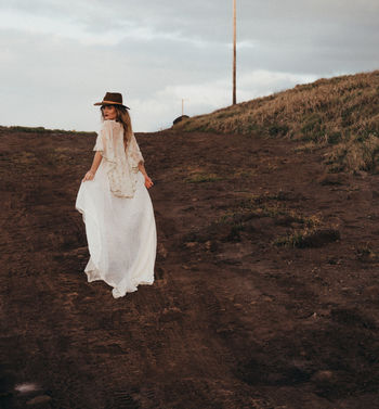 Woman wearing white dress while walking on land against sky