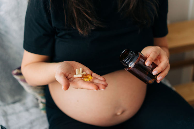 Unrecognizable pregnant woman holds vitamin capsules in her palm.