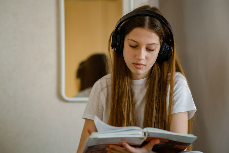 Young teenage girl in headphones with a textbook in her hands.