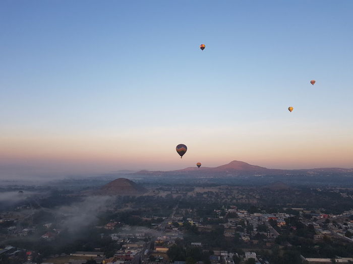 Hot air balloons flying in city against sky during sunrise