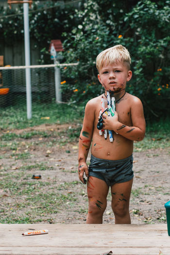 Portrait of shirtless boy standing outdoors with markers.