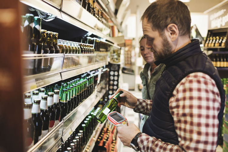 Man using bar code reader on beer bottle while standing with woman in supermarket