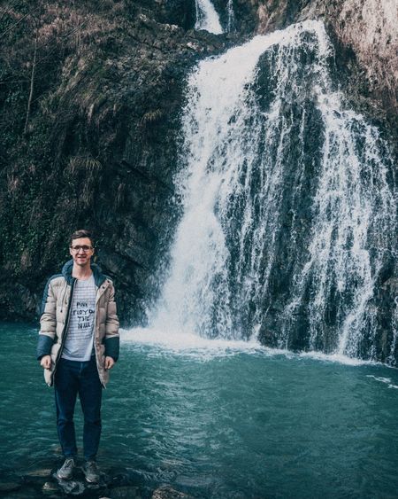 Full length portrait of young man standing on rock against waterfall