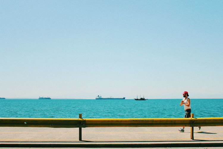 Side view of man running on pier by sea against clear sky