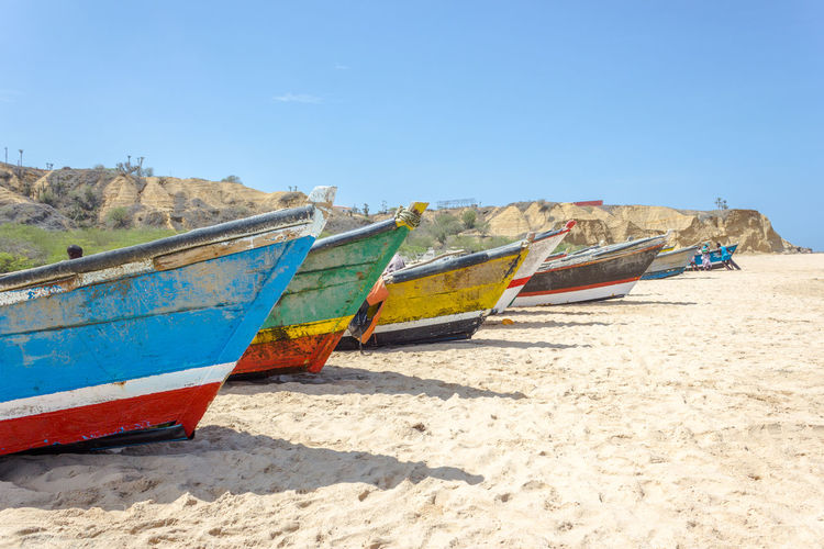 Boats moored on beach against clear blue sky