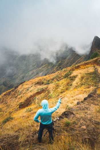 High angle view of man gesturing while standing on cliff during foggy mountain