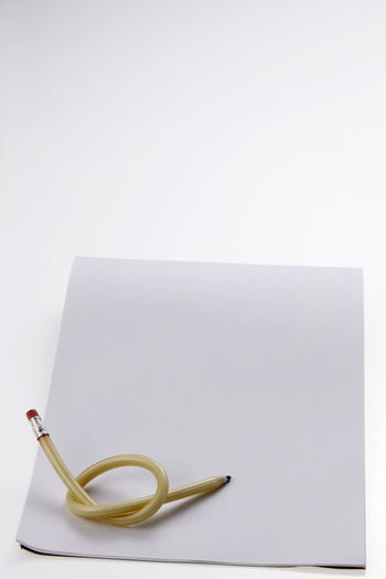 Close-up of knotted pencil and book against white background