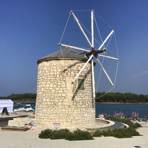 Traditional windmill at beach against clear sky