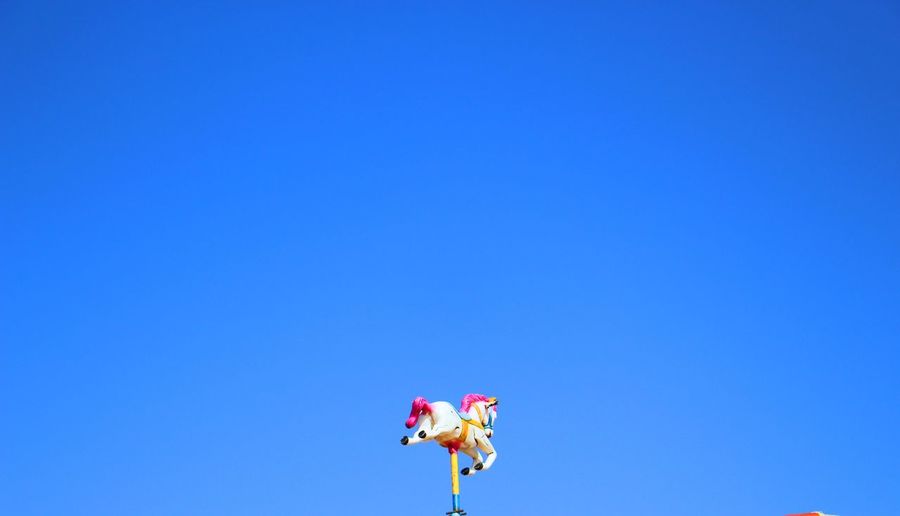 Low angle view of carousel horse against clear blue sky