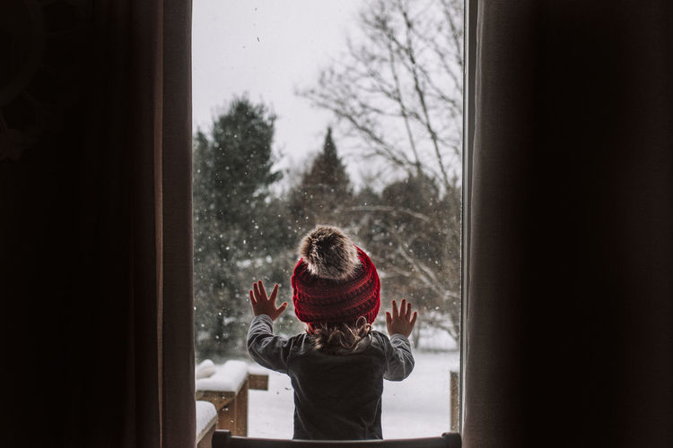Little girl looks out the window during a snow day in the winter