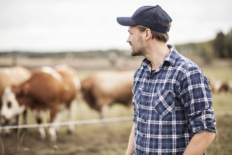 Thoughtful farmer standing on field while animals grazing in background