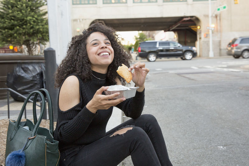 Young woman eating outside a grocery store in queens, new york