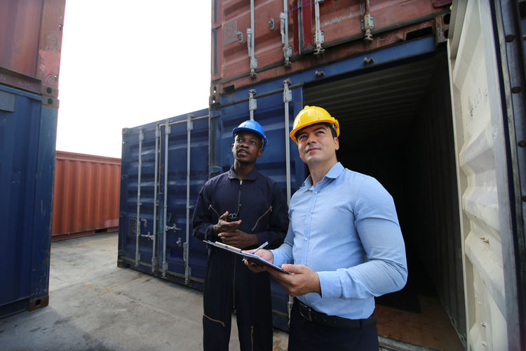YOUNG MAN HOLDING CAMERA WHILE STANDING AT OFFICE