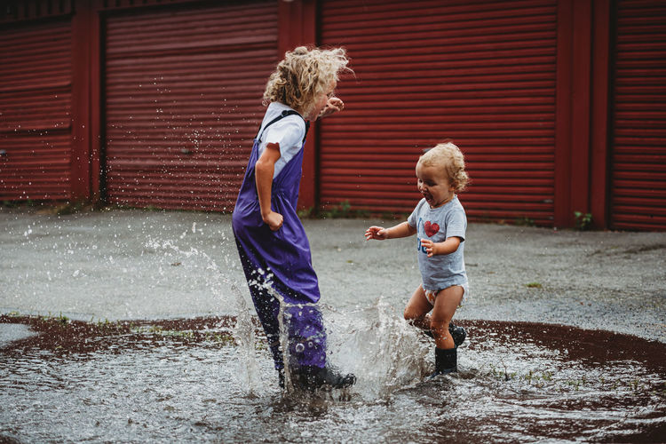 Girl and boy splashing in the water after the rain and laughing