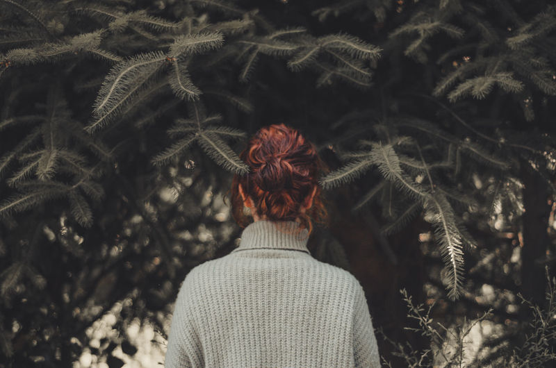 Rear view of woman standing amidst plants during winter