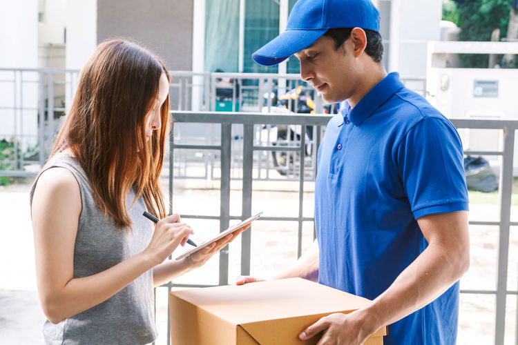 Woman signing on digital tablet while salesman holding cardboard box