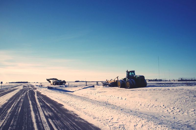Snowplow on field by road against clear blue sky