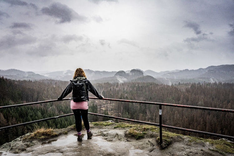 Rear view of woman standing on footbridge against sky