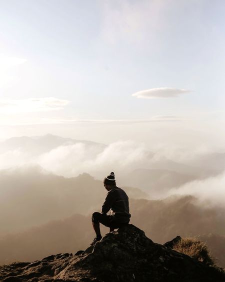 Man sitting on rock against mountains against sky