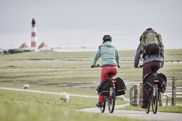 Germany, schleswig-holstein, eiderstedt, couple riding bicycle near westerheversand lighthouse