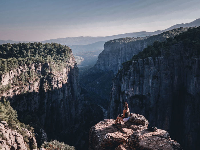 Girl sitting on rock by mountains against sky