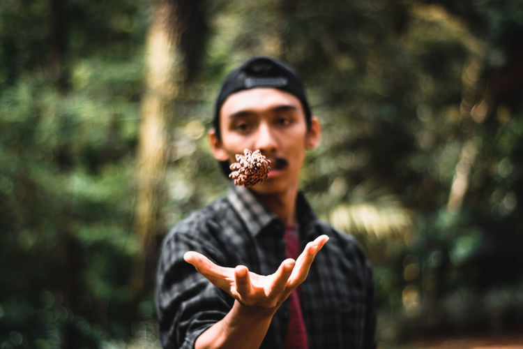 Close-up of man catching pine cone against trees