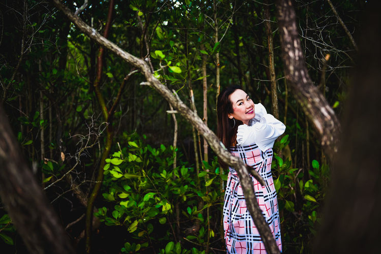 Young woman standing by tree in forest