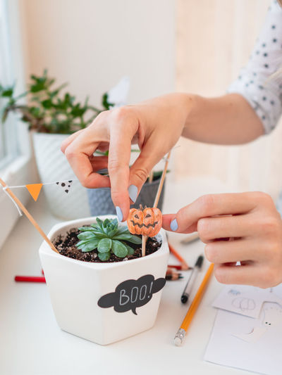 Woman decorates flower pots with handmade stickers for halloween. hand drawn pumpkin and flags.