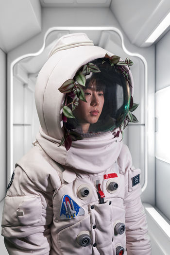 Asian woman in astronaut costume and helmet with green vine looking away during space mission in spaceship