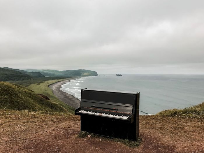 Piano on mountain by sea against cloudy sky