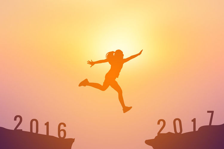 Silhouette girl jumping amidst rocks with numbers against sky during sunset