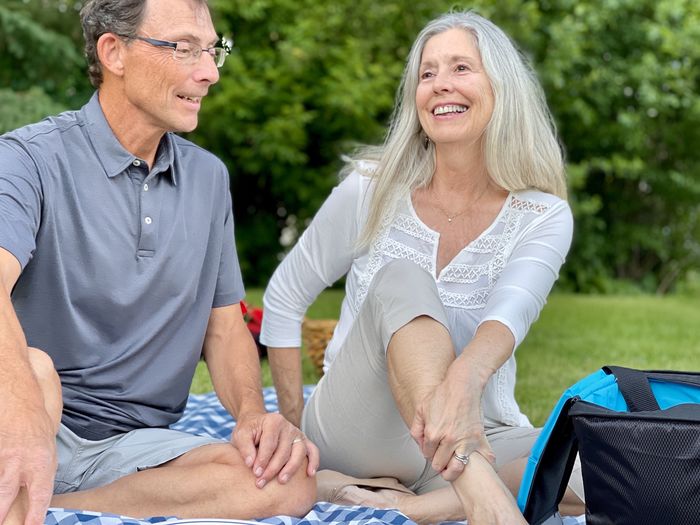 Happy senior couple enjoying picnic together seated on blue checked blanket against trees.  portrait