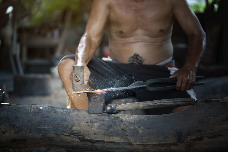 Midsection of shirtless manual worker working at workshop
