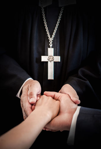 Midsection of priest holding couple hands during wedding