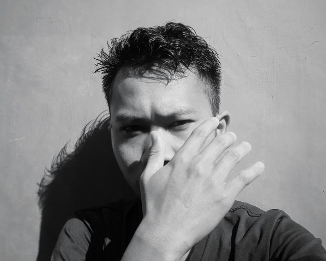 Close-up portrait of young man covering face against wall