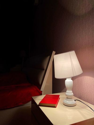 Illuminated electric lamp on table by wall at home