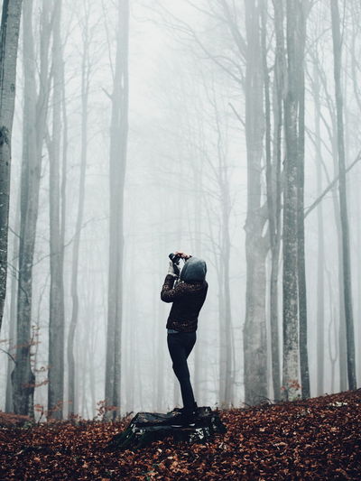 Woman photographing in forest during foggy weather