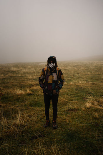 Full length portrait of young woman standing on field with fog
